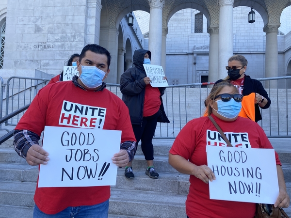Hospitality workers hold signs reading "Good jobs now!!" and "Good housing now!!" outside Los Angeles City Hall