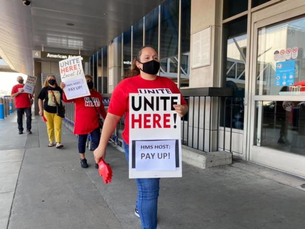 Workers picket at LAX wearing signs that say, "HMS Host: Pay Up!"