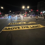 Large yellow banners lie in the center of the busy intersection at Century Boulevard and Avion Drive near LAX. The banners read, "City of LA: Why is Flying Food Group above the law?"