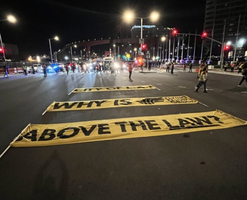 Large yellow banners lie in the center of the busy intersection at Century Boulevard and Avion Drive near LAX. The banners read, "City of LA: Why is Flying Food Group above the law?"