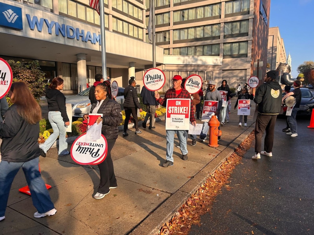 On a beautiful November day outside a building marked "Wyndham" in blue letters, striking workers picket with signs reading "ON STRIKE! at Wyndham Philadelphia" and "Philly UNITE HERE Local 274"