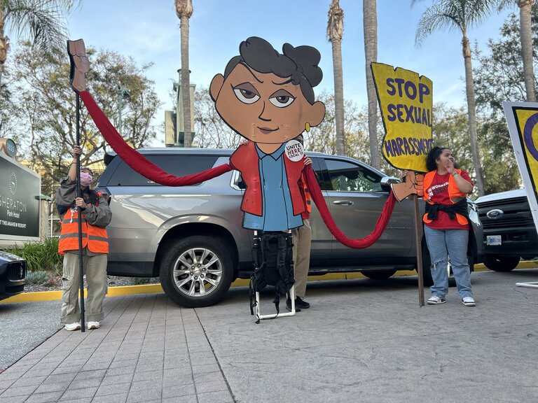 Hotel workers use an 8-foot tall puppet of a woman with a picket sign to protest sexual harassment complaints outside the Aimbridge-operated Sheraton Park Anaheim 2024-03-13.