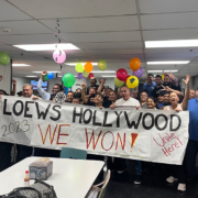 A group of 50 hotel workers with balloons stand behind a banner that reads "Loews Hollywood: We Won!"