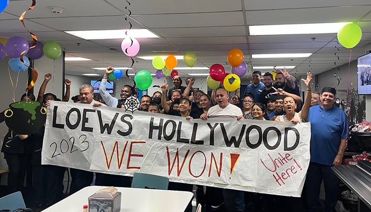 A group of 50 hotel workers with balloons stand behind a banner that reads "Loews Hollywood: We Won!"