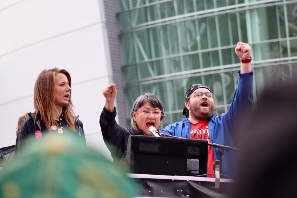 Nicole Miller, president of IATSE B-192, Susan Minato, co-president of UNITE HERE Local 11, and Chris Lillian, a food service worker at Universal Studios Hollywood, speak from an outdoor stage in downtown Los Angeles.
